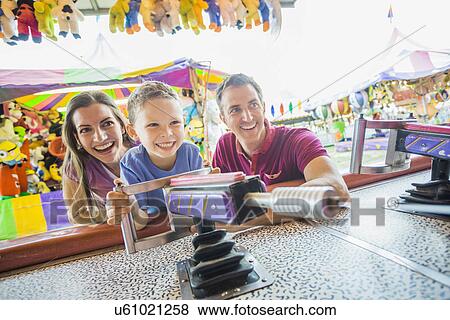 Stock Photo - Happy Family with son (4-5) playing with water gun in amusement park. Fotosearch