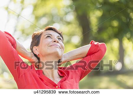 Stock Photo - Happy mature woman raising hands in park. Fotosearch