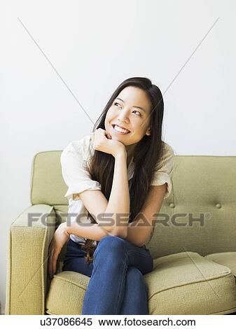 Stock Photography - Happy young woman sitting on sofa. Fotosearch