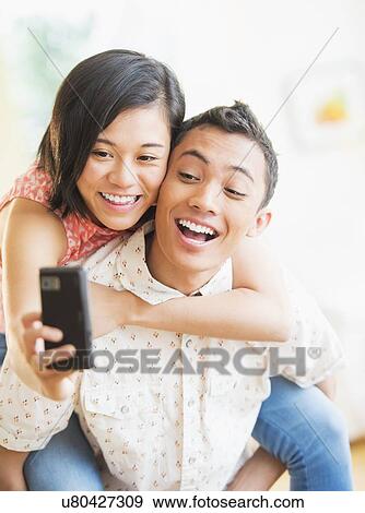 Stock Photo - Man giving piggy back ride to woman photographing. Fotosearch