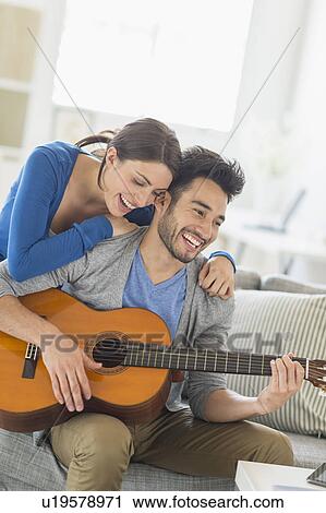 Stock Image - Man playing guitar while woman embracing him. Fotosearch