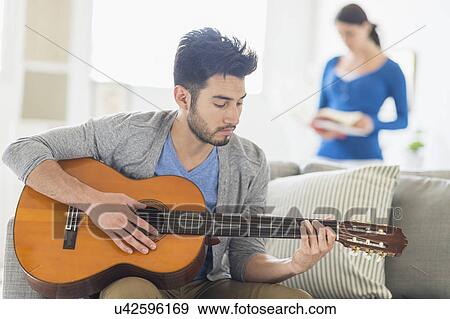 Stock Photo - Man playing guitar, woman in background. Fotosearch