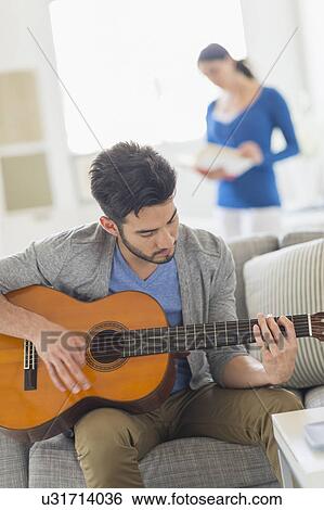 Stock Photograph - Man playing guitar, woman in background. Fotosearch