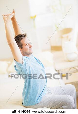Picture - Man sitting on bed and stretching. Fotosearch