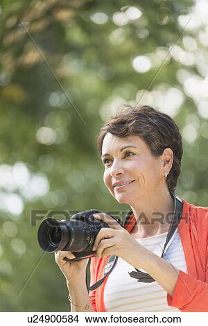 Mature woman holding camera in park View Large Photo Image Picture - Mature woman holding camera in park. Fotosearch