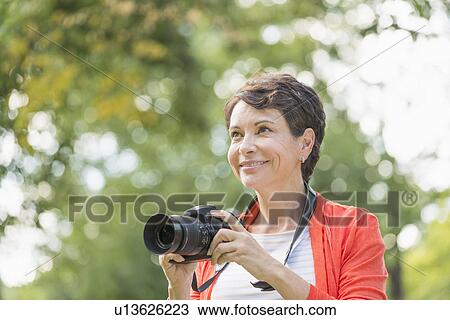 Mature woman holding camera in park View Large Photo Image Stock Image - Mature woman holding camera in park. Fotosearch
