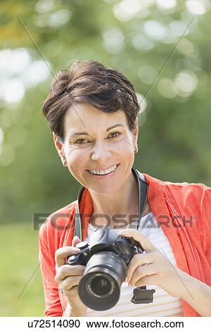 Mature woman holding camera in park View Large Photo Image Stock Image - Mature woman holding camera in park. Fotosearch