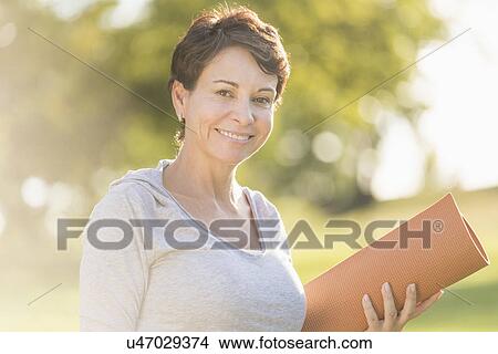 Mature woman holding yoga mat outdoors View Large Photo Image Picture - Mature woman holding yoga mat outdoors. Fotosearch