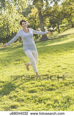 Stock Image - Mature woman jumping on grass. Fotosearch