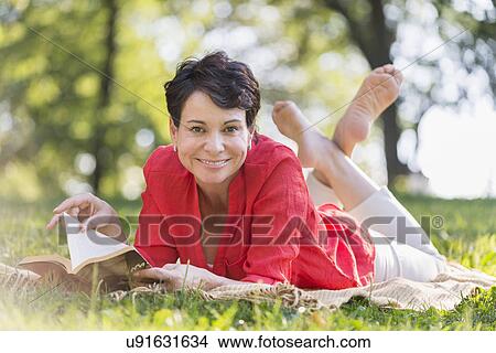 Picture - Mature woman lying on grass and reading book. Fotosearch
