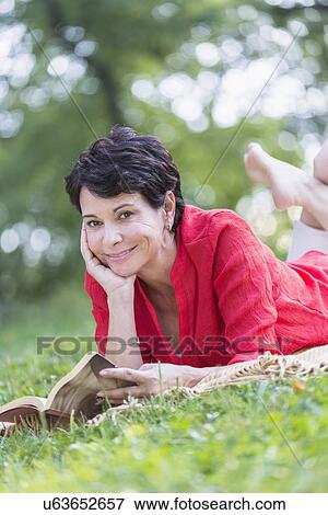 Mature woman lying on grass and reading book View Large Photo Image Stock Photo - Mature woman lying on grass and reading book. Fotosearch