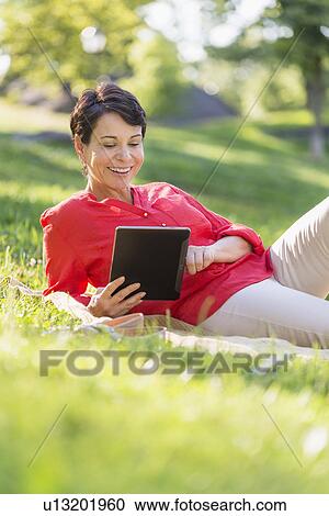 Mature woman lying on grass and using digital tablet View Large Photo Image Stock Image - Mature woman lying on grass and using digital tablet. Fotosearch