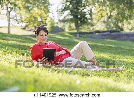 Mature woman lying on grass and using digital tablet View Large Photo Image Stock Photography - Mature woman lying on grass and using digital tablet. Fotosearch