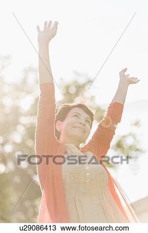 Stock Image - Mature woman raising hands in sunlight. Fotosearch
