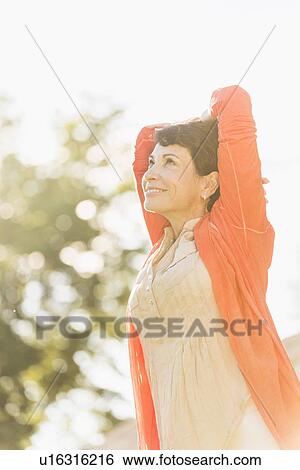 Stock Photograph - Mature woman raising hands in sunlight. Fotosearch