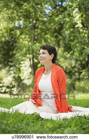 Stock Image - Mature woman sitting on grass in park. Fotosearch