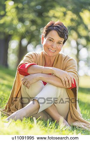 Stock Photography - Mature woman sitting on grass in park. Fotosearch