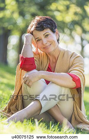 Mature woman sitting on grass in park View Large Photo Image Stock Photography - Mature woman sitting on grass in park. Fotosearch