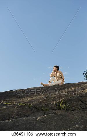 Stock Photography - Mature woman sitting on rock. Fotosearch