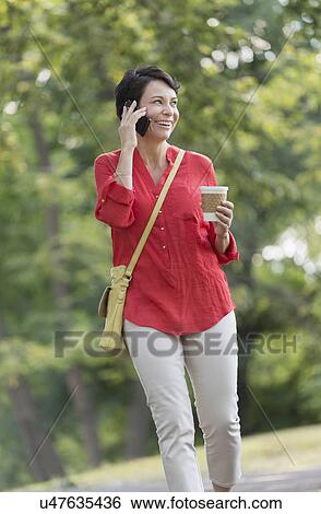 Mature woman talking on cell phone in park View Large Photo Image Stock Photograph - Mature woman talking on cell phone in park. Fotosearch