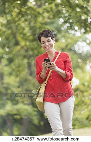 Stock Photo - Mature woman text messaging in park. Fotosearch