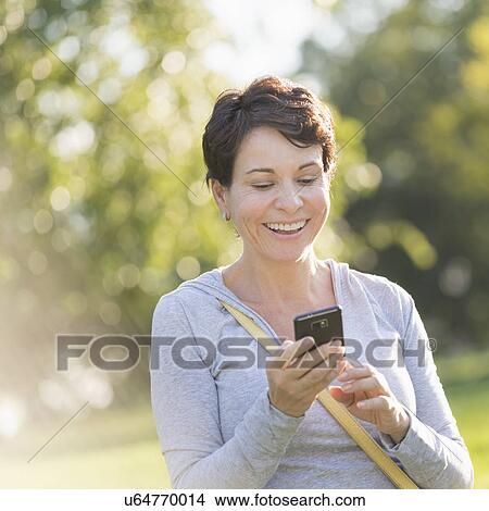 Picture - Mature woman text messaging outdoors. Fotosearch