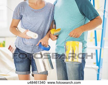 Stock Image - Mid section of couple with paint rollers and paint cans. Fotosearch