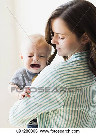 Stock Image - Mother consoling baby boy (6-11 months) indoors. Fotosearch