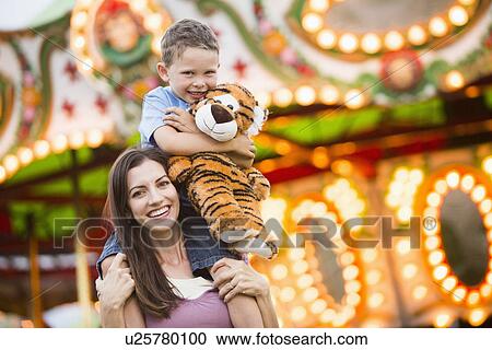 Stock Image - Mother giving her son (4-5) piggyback ride in amusement park. Fotosearch