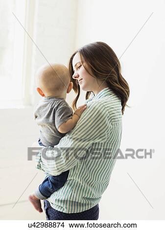Picture - Mother holding baby boy (6-11 months) indoors. Fotosearch