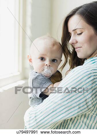 Stock Image - Mother holding baby boy (6-11 months) indoors. Fotosearch