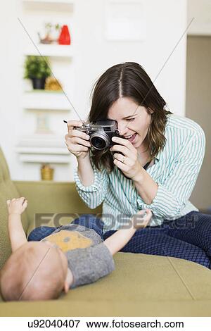 Mother sitting on sofa photographing baby boy (6-11 months) View Large Photo Image Stock Photo - Mother sitting on sofa photographing baby boy (6-11 months). Fotosearch