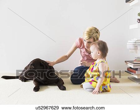 Mother with baby daughter (12-17 months) playing with dog View Large Photo Image Stock Photo - Mother with baby daughter (12-17 months) playing with dog. Fotosearch