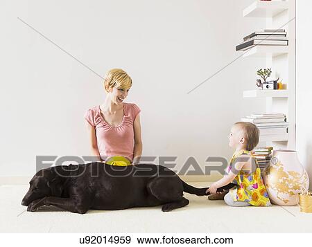Mother with baby daughter (12-17 months) playing with dog View Large Photo Image Stock Photo - Mother with baby daughter (12-17 months) playing with dog. Fotosearch