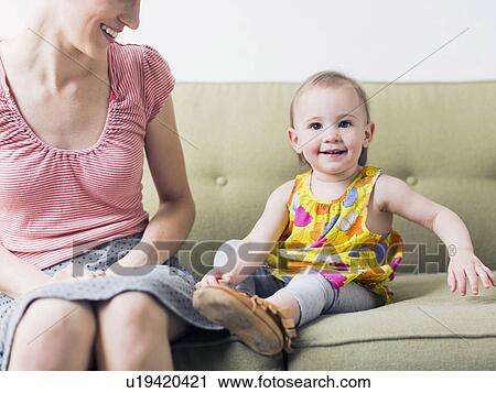 Stock Image - Mother with daughter (12-17 months) sitting on sofa. Fotosearch