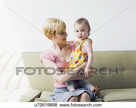 Mother with daughter (12-17 months) sitting on sofa View Large Photo Image Stock Photo - Mother with daughter (12-17 months) sitting on sofa. Fotosearch