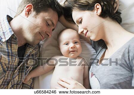 Parents and baby son (2-5 months) lying on bed View Large Photo Image Stock Photograph - Parents and baby son (2-5 months) lying on bed. Fotosearch