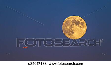 Stock Photo - Plane flying across clear sky with full moon. Fotosearch