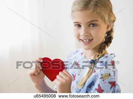 Stock Photo - Portrait of blond girl (8-9) in hospital with paper heart. Fotosearch