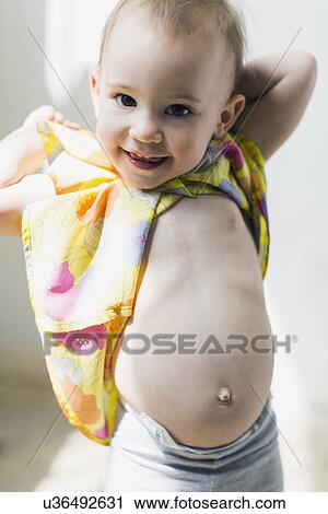 Stock Image - Portrait of girl (12-17 months) showing bellybutton. Fotosearch