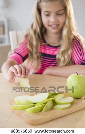 Stock Image - Portrait of girl (8-9) eating apple. Fotosearch