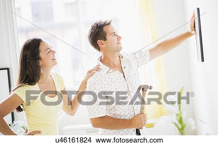 Picture - Portrait of happy couple hanging picture. Fotosearch