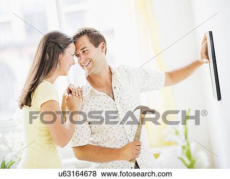 Stock Photo - Portrait of happy couple hanging picture. Fotosearch