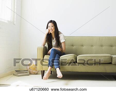 Stock Image - Portrait of happy young woman sitting on sofa. Fotosearch