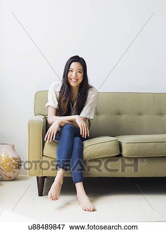 Portrait of happy young woman sitting on sofa View Large Photo Image Stock Photo - Portrait of happy young woman sitting on sofa. Fotosearch