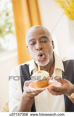 Portrait of man holding cupcake and blowing out candle View Large Photo Image Stock Photo - Portrait of man holding cupcake and blowing out candle. Fotosearch