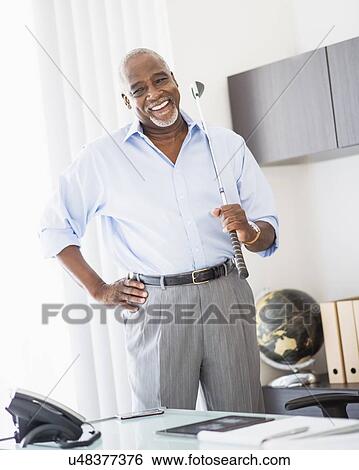 Stock Photograph - Portrait of man in office holding golf club. Fotosearch
