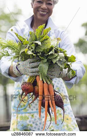 Stock Photo - Portrait of senior woman holding carrots and beetroot. Fotosearch