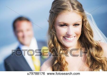 Stock Photograph - Portrait of smiling bride, groom in background. Fotosearch