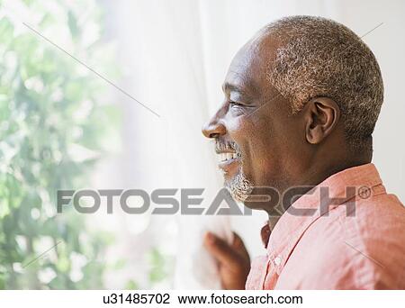 Stock Image - Portrait of smiling man looking through window. Fotosearch